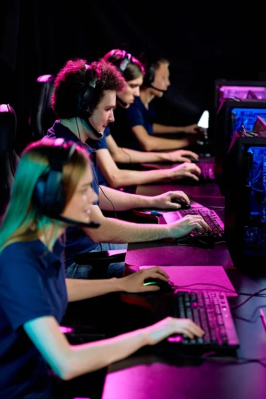 Fila de jogadores de eSports com auscultadores de jogos, a competir em computadores de secretária durante uma sessão de jogo multijogador numa arena de jogos profissional.