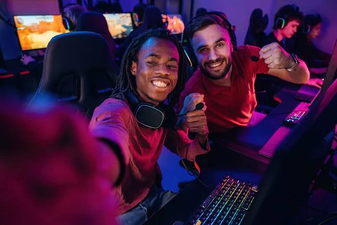 Dois jogadores sorridentes a celebrar uma partida multijogador bem-sucedida, com auscultadores de jogos, num moderno centro de eSports, enquanto tiram uma selfie.